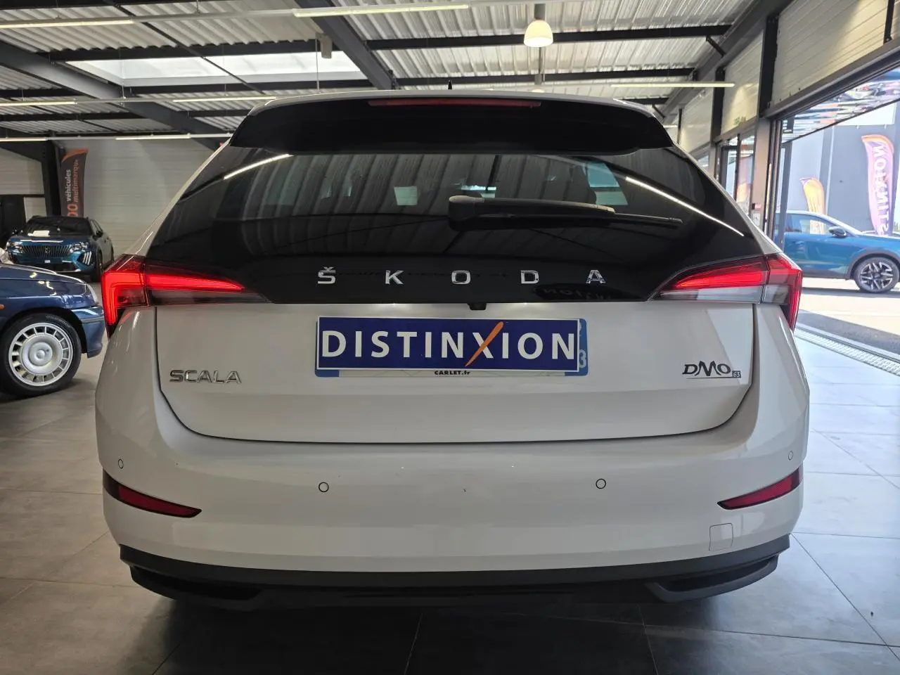 Vue arrière d'une Skoda Scala blanche avec feux LED et hayon noir dans un showroom.