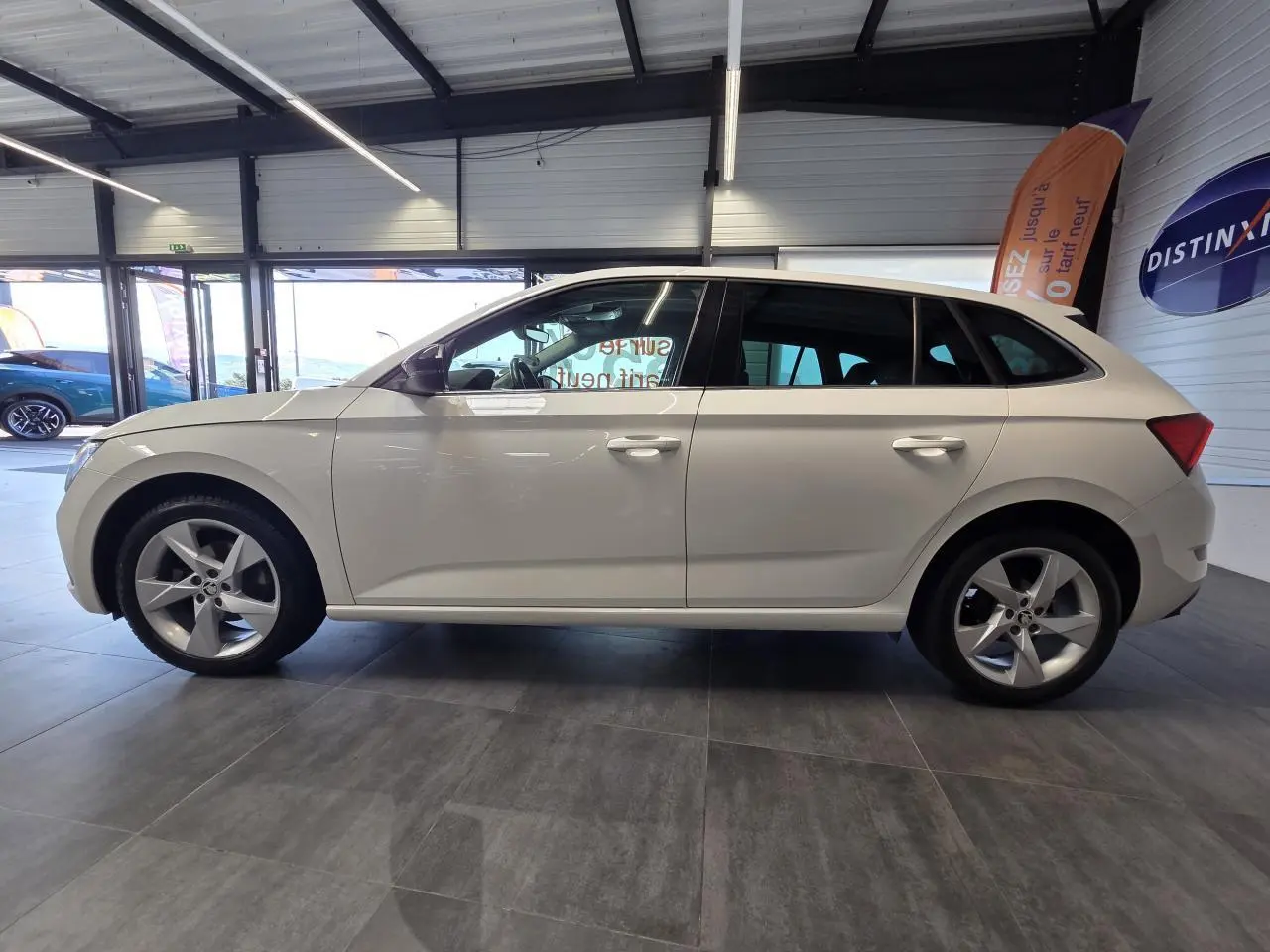 Vue de profil côté gauche d'une Skoda Scala blanche 2020 avec jantes alliage 17 pouces dans un showroom.