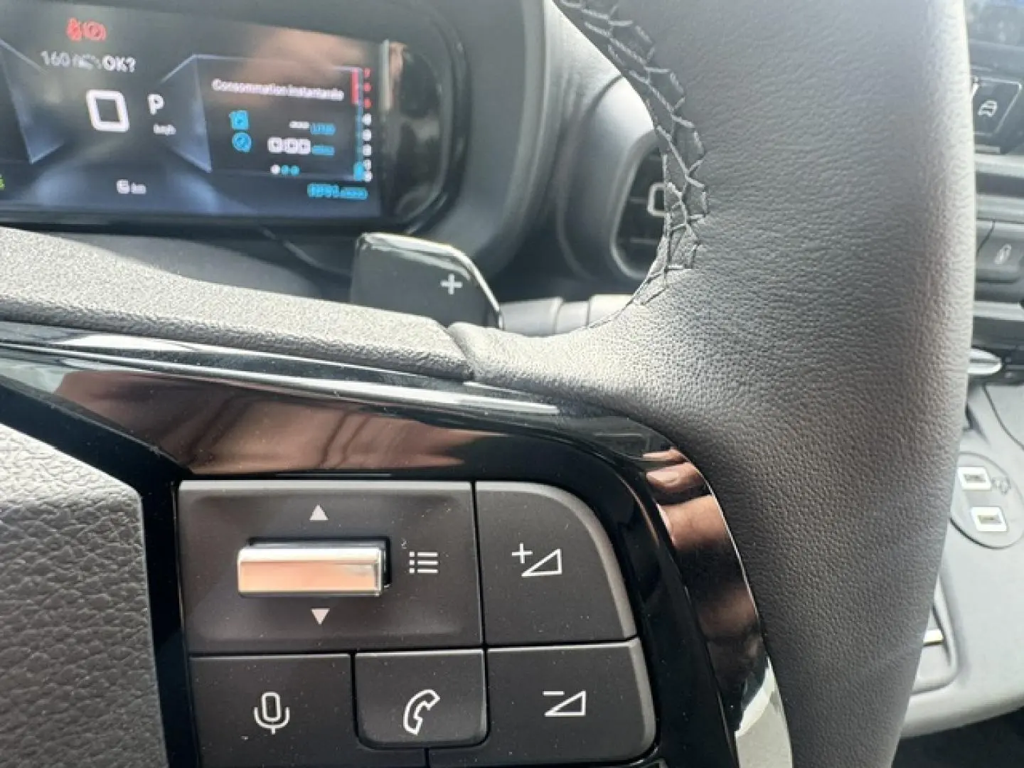 Gros plan sur les commandes au volant cuir noir du Citroën Berlingo 2026, affichage numérique en arrière-plan.