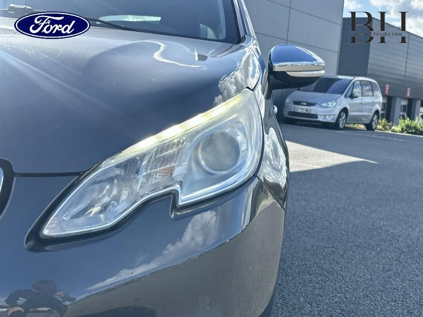 Gros plan sur le phare avant droit d'un Peugeot 2008 Spirit Grey, avec rétroviseur chromé et reflet du ciel.