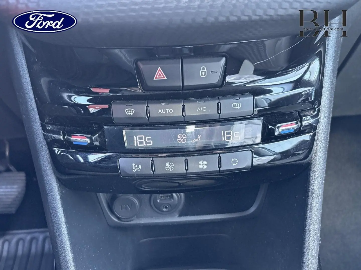 Console centrale noire avec commandes climatisation automatique bi-zone et prises 12V dans un Ford, vue rapprochée frontale.