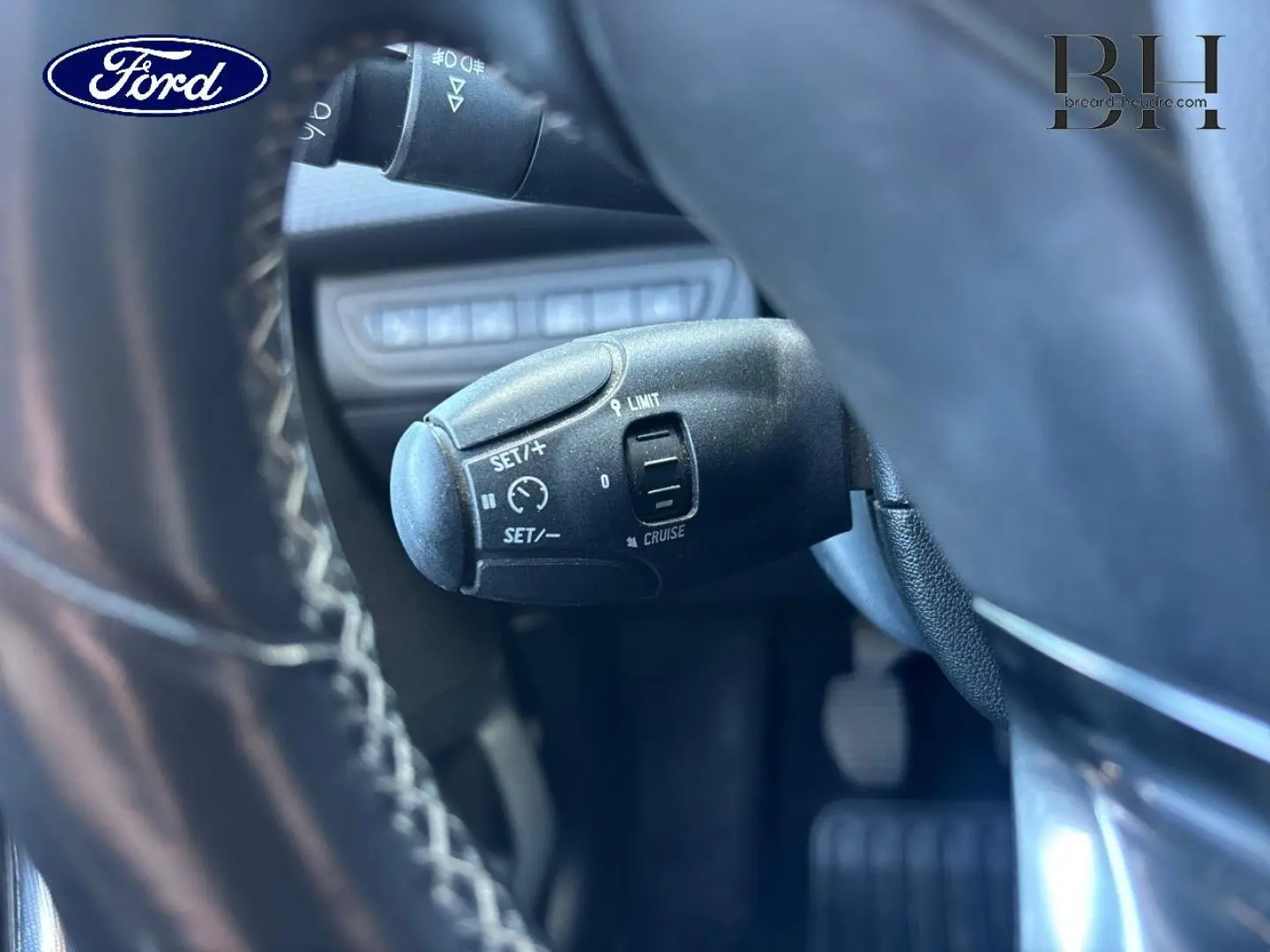 Gros plan sur la commande de régulateur de vitesse noire, vue depuis le volant d’un véhicule Ford.