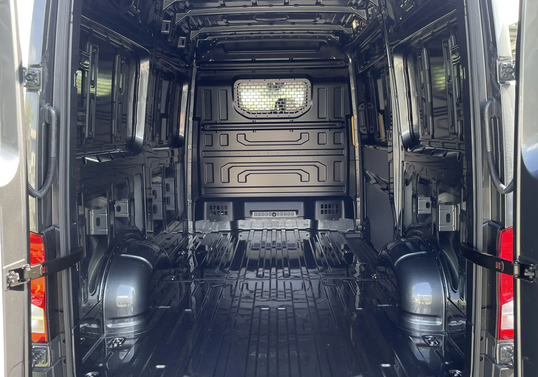 Intérieur du coffre ouvert d'un Volkswagen Crafter gris Indium, montrant la cloison avec vitre fixe et l'espace de chargement vide.