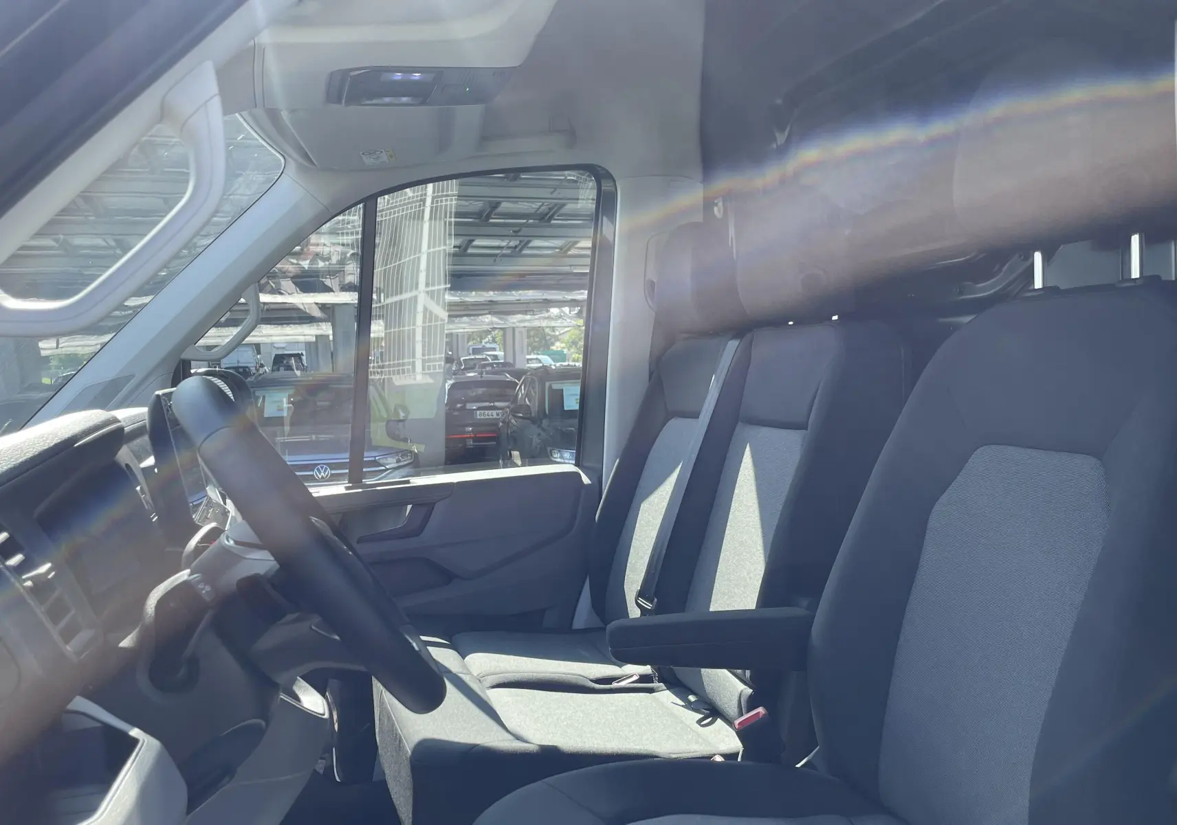 Vue intérieure côté conducteur du Volkswagen Crafter Van 2025 avec sièges tissu gris et cloison vitrée arrière.