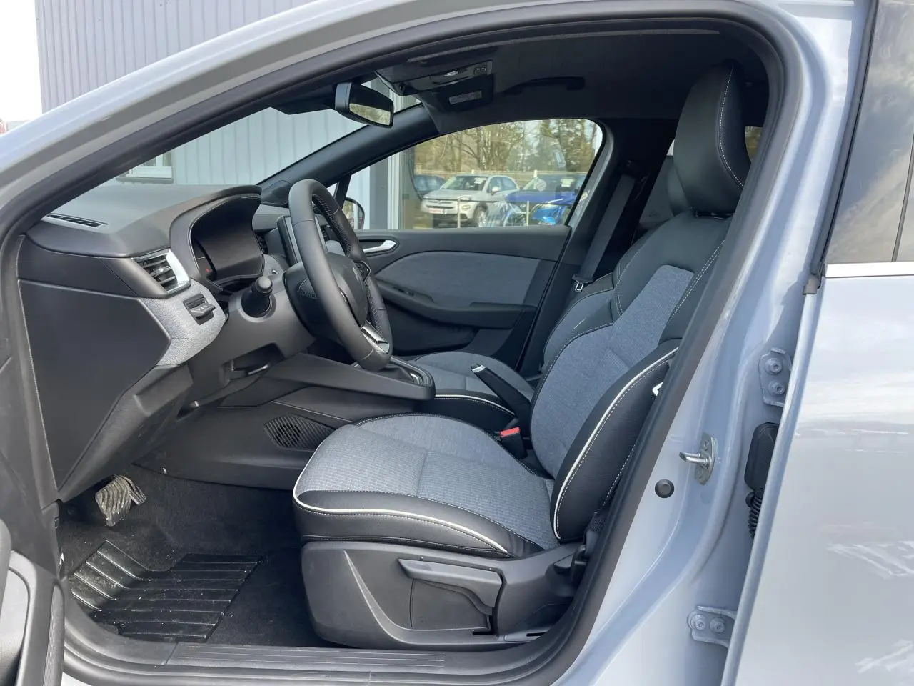 Vue côté gauche de l'intérieur de la Renault Clio Gris Rafale 2025, sièges tissu gris et volant multifonction.