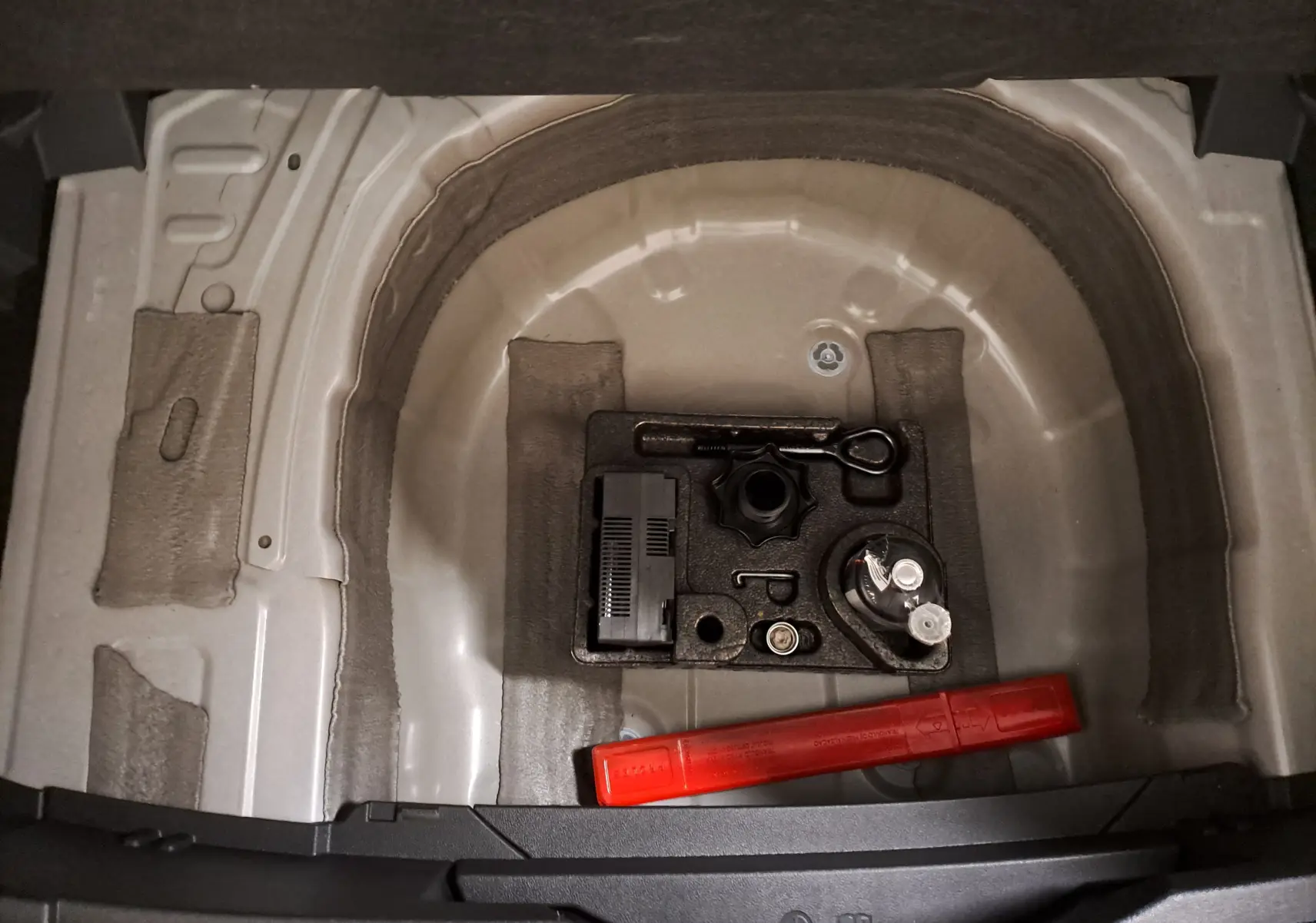 Coffre ouvert du Volkswagen T-Cross blanc, vue plongeante sur le rangement sous plancher avec outils et triangle de signalisation rouge.