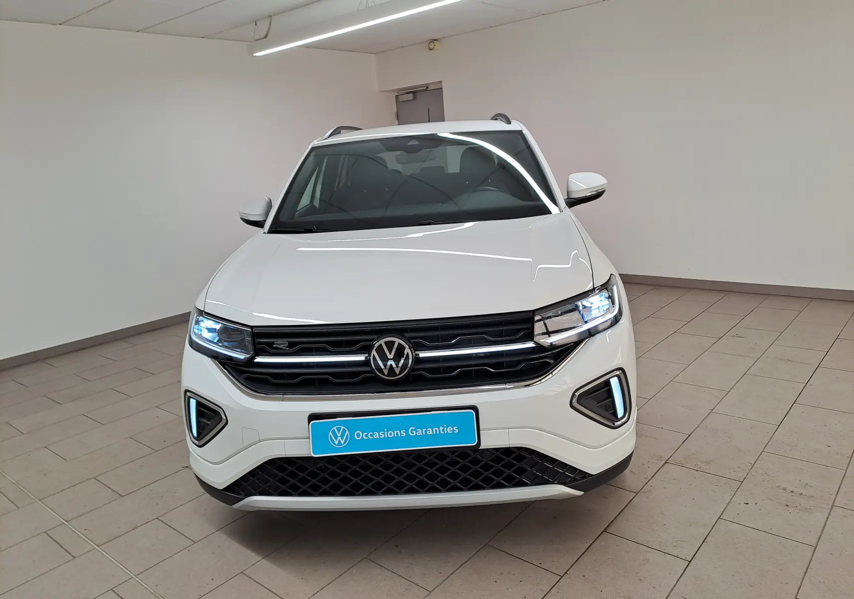 Volkswagen T-Cross blanc pur 2025 en vue 3/4 avant droit, avec jantes R-Line et phares LED allumés.