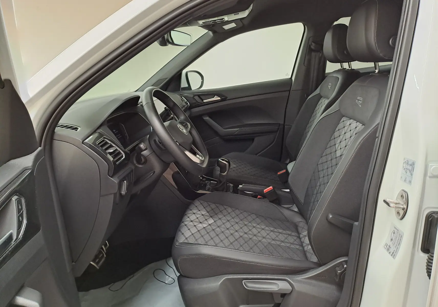 Vue intérieure côté conducteur du Volkswagen T-Cross blanc 2025, sièges R-Line avec surpiqûres et volant multifonction.