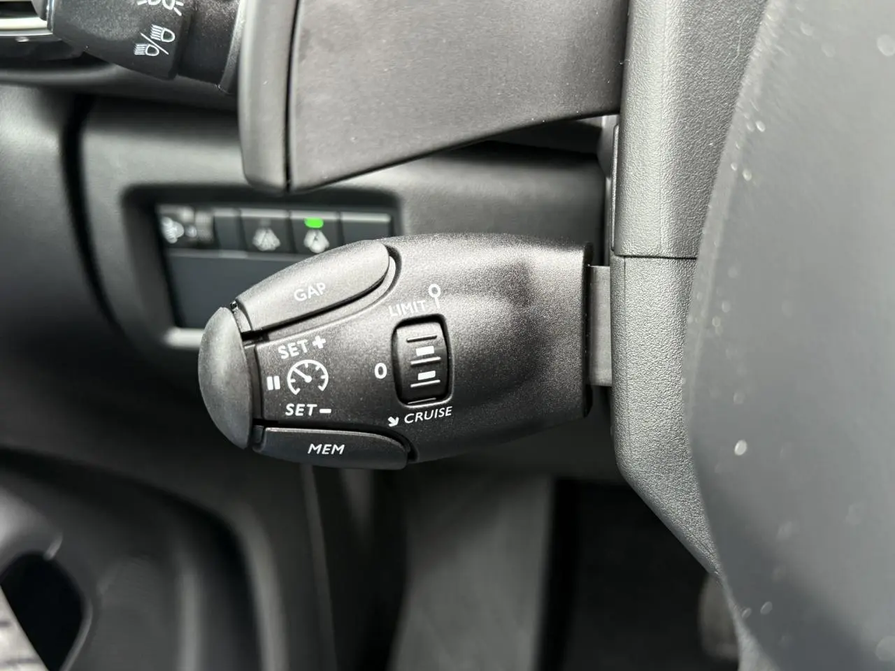 Gros plan sur la commande de régulateur de vitesse à gauche du volant dans l'habitacle noir du Citroën C5 Aircross 2025.