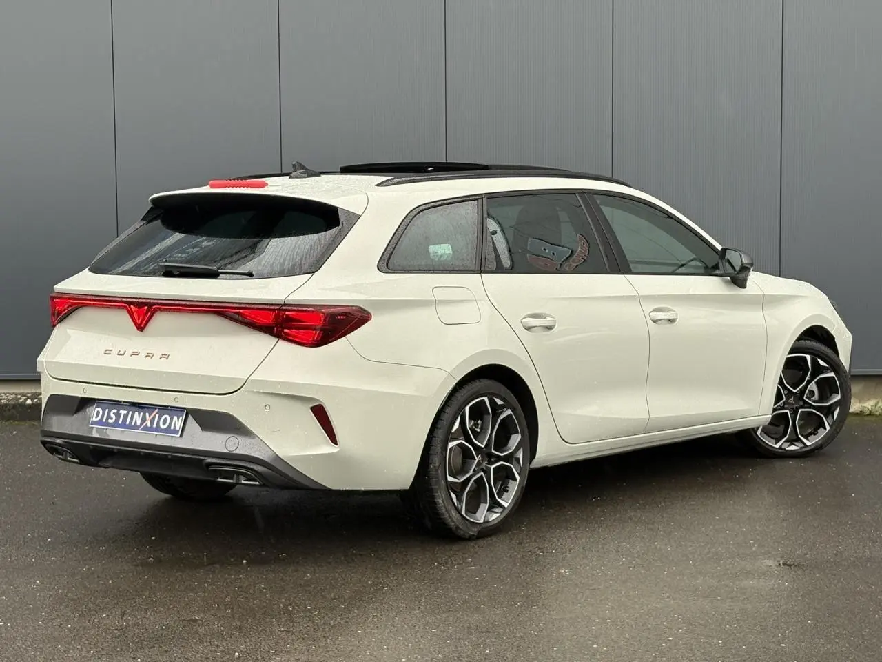Vue 3/4 arrière droite d'une CUPRA Leon ST 2025 blanche avec toit noir et jantes alliage distinctives.