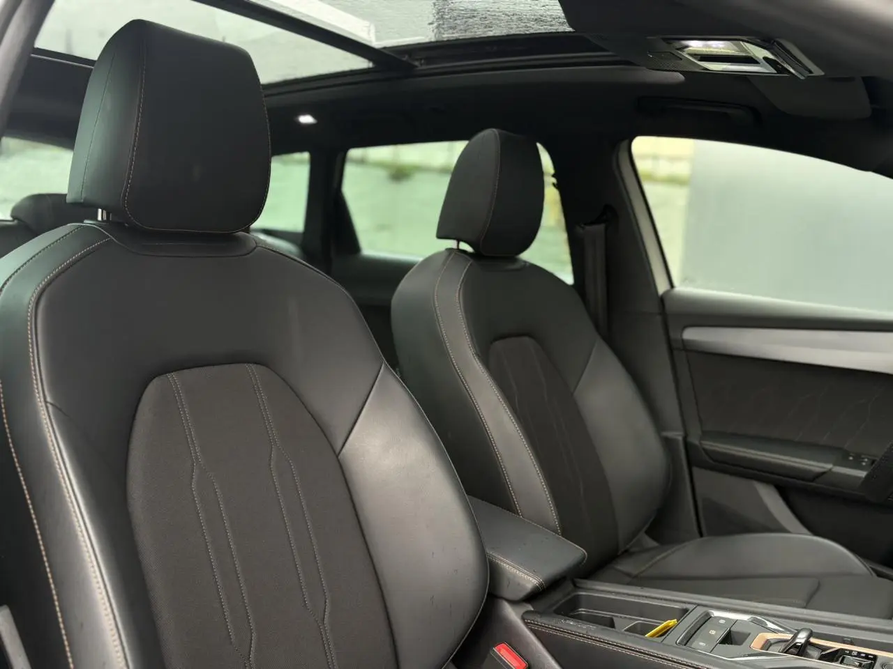 Vue intérieure avant des sièges en cuir noir du CUPRA LEON ST 2025 avec toit ouvrant panoramique visible.