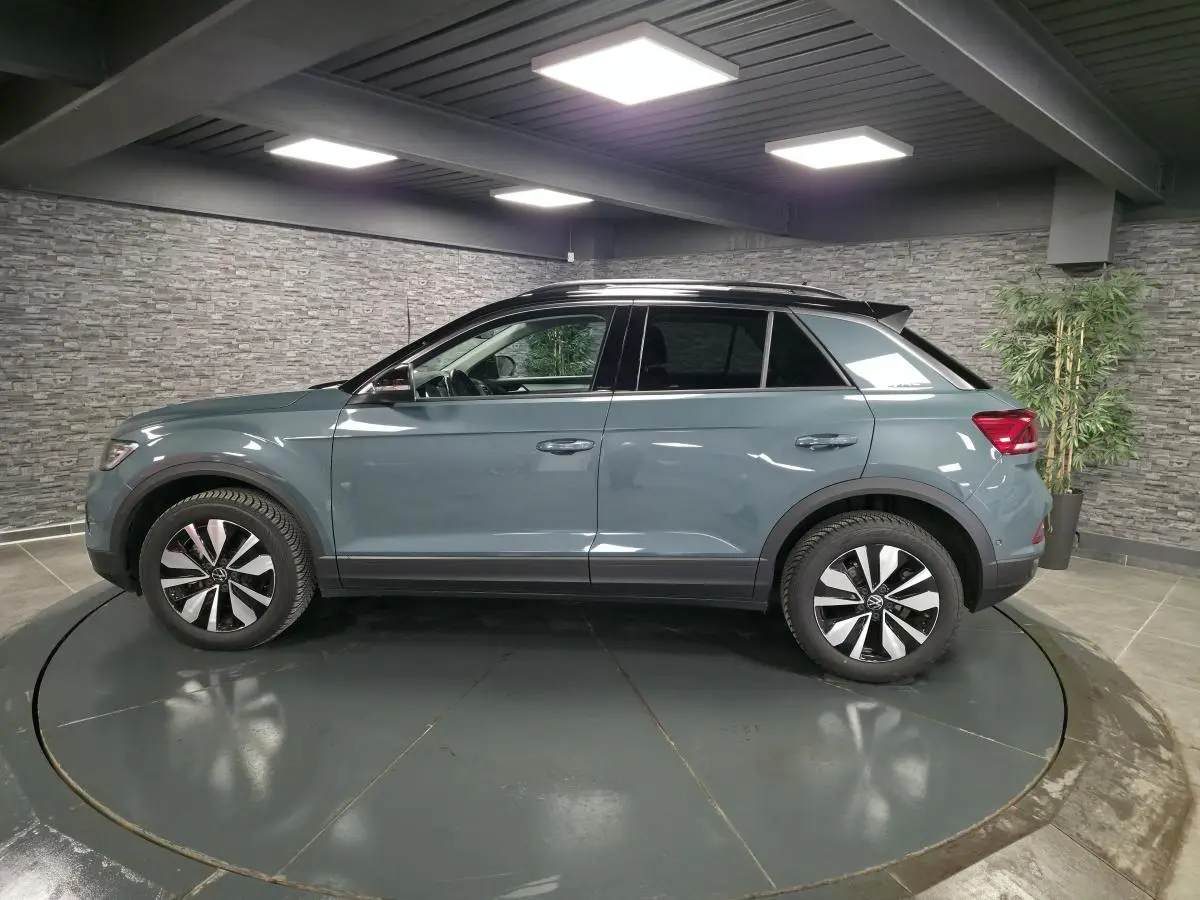 Vue de profil côté gauche d'un Volkswagen T-Roc bleu métallisé avec toit noir dans un showroom.