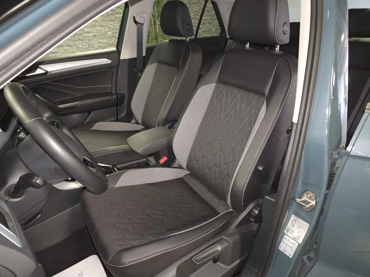 Vue intérieure côté conducteur du Volkswagen T-Roc 2025 bleu, sièges tissu noir et gris avec surpiqûres blanches.