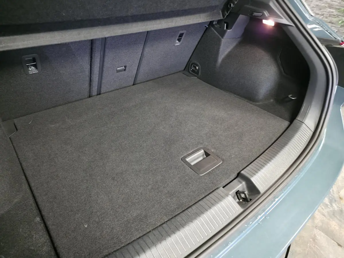 Vue intérieure du coffre spacieux du Volkswagen T-Roc bleu, avec tapis gris foncé et éclairage latéral.