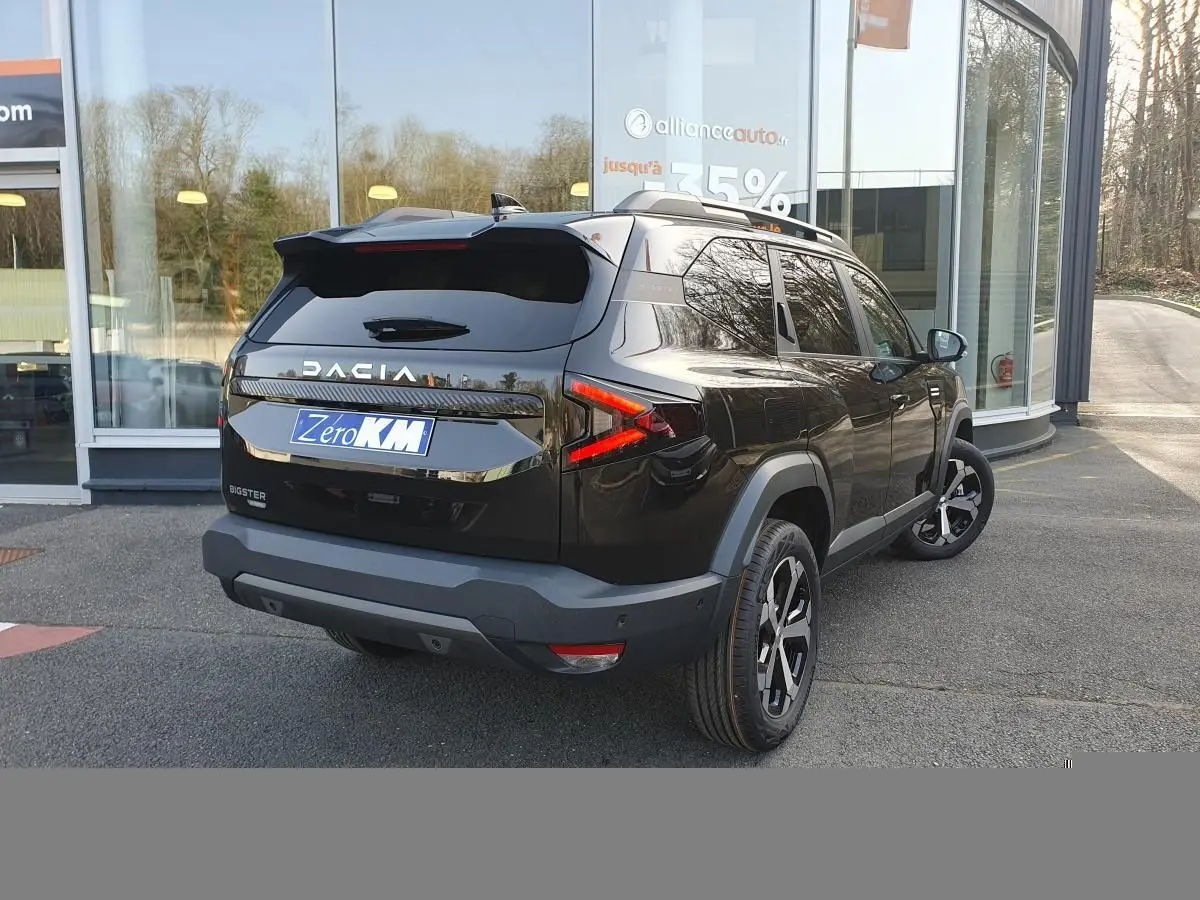 Vue 3/4 arrière droite du Dacia Bigster noir Perla avec jantes alliage 18” diamantées et barres de toit longitudinales.