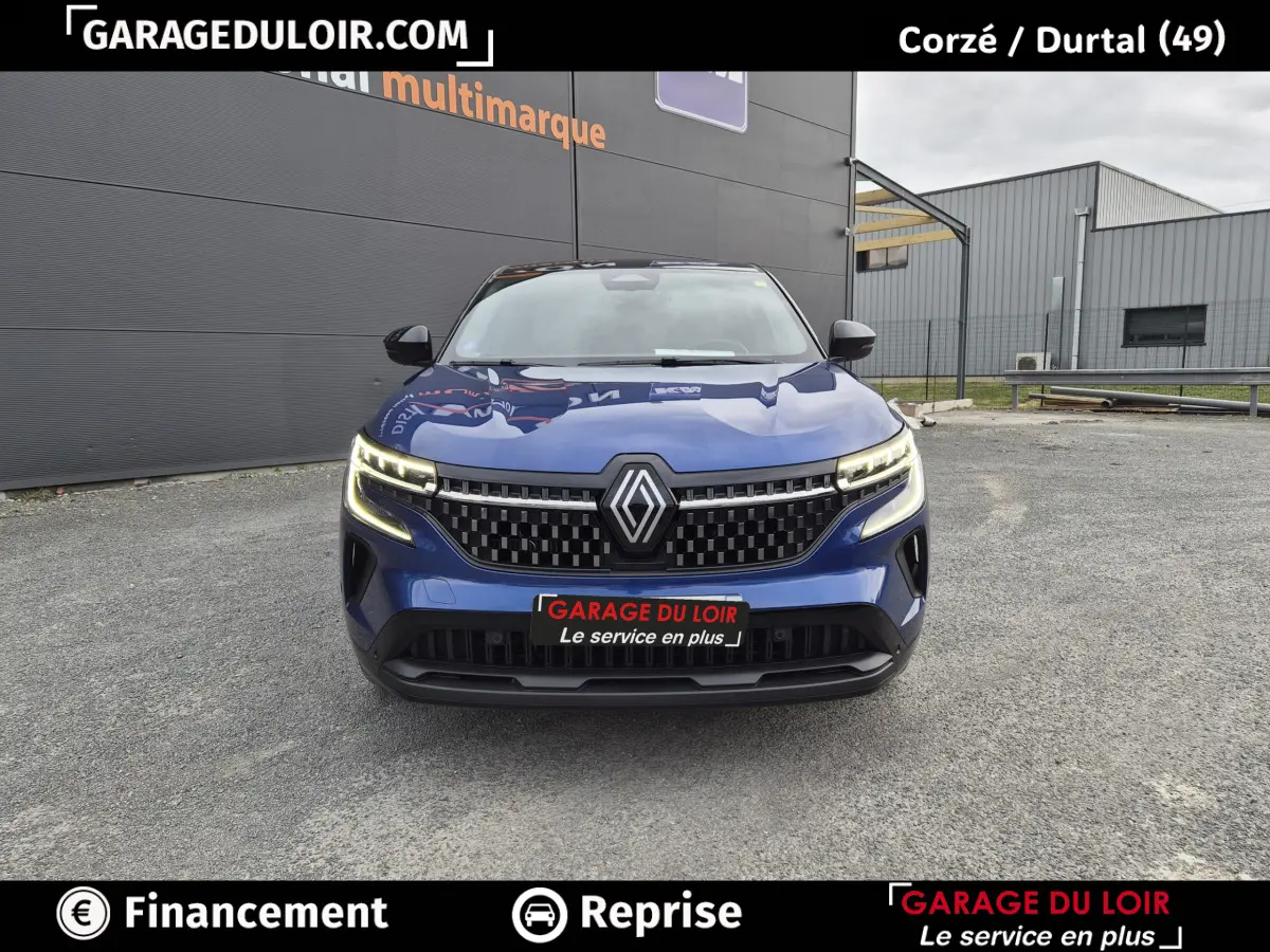 Vue avant d'un Renault Austral bleu avec calandre noire à damier et feux LED allumés sur parking extérieur.