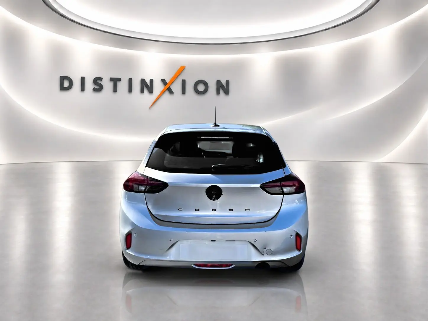Vue arrière d'une Opel Corsa gris clair 2025 dans un showroom avec éclairage moderne et logo Distinxion en arrière-plan.