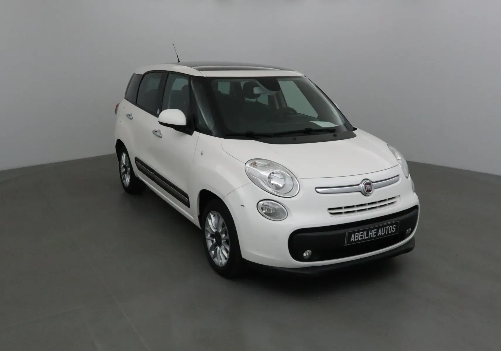 Fiat 500L blanc vue 3/4 avant droit dans un studio, avec toit ouvrant et jantes alliage visibles.