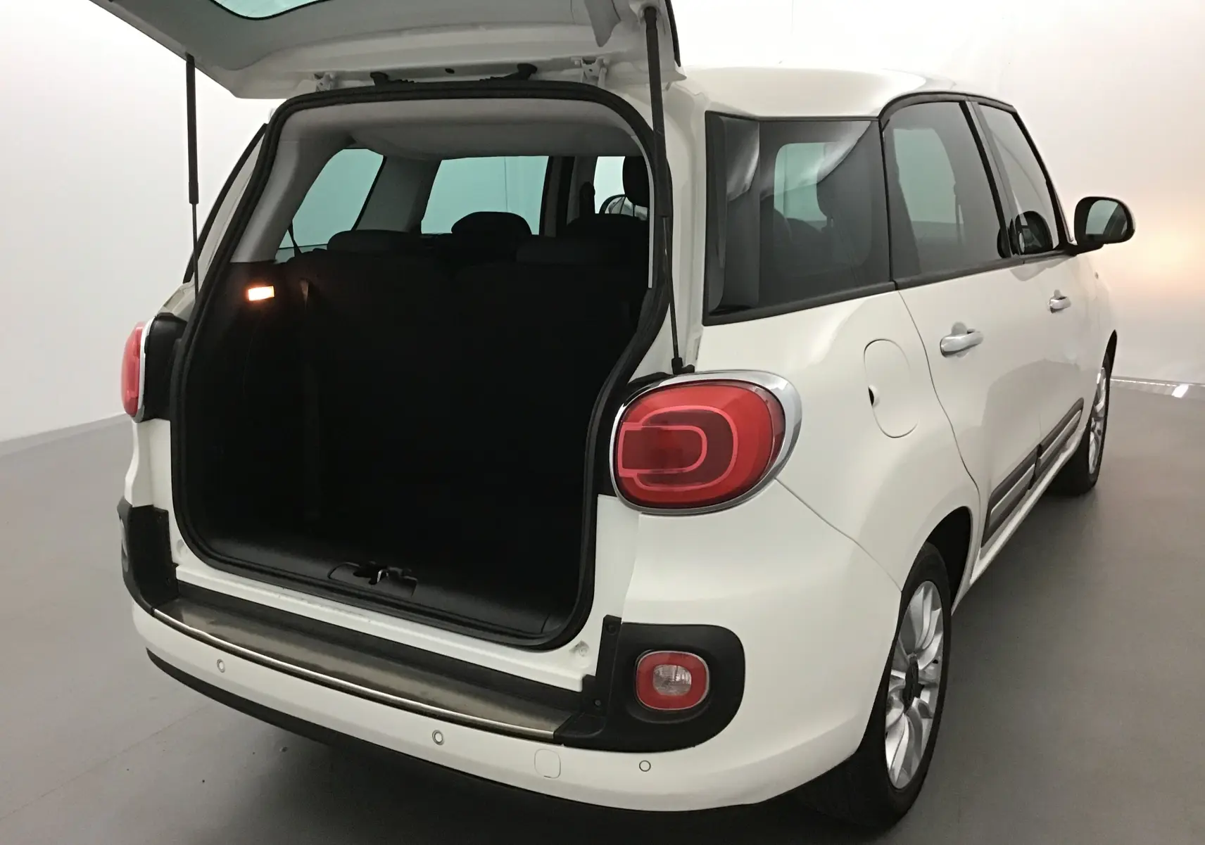 Vue 3/4 arrière droite d'une FIAT 500L blanche avec coffre ouvert et lunette arrière surteintée dans un studio.