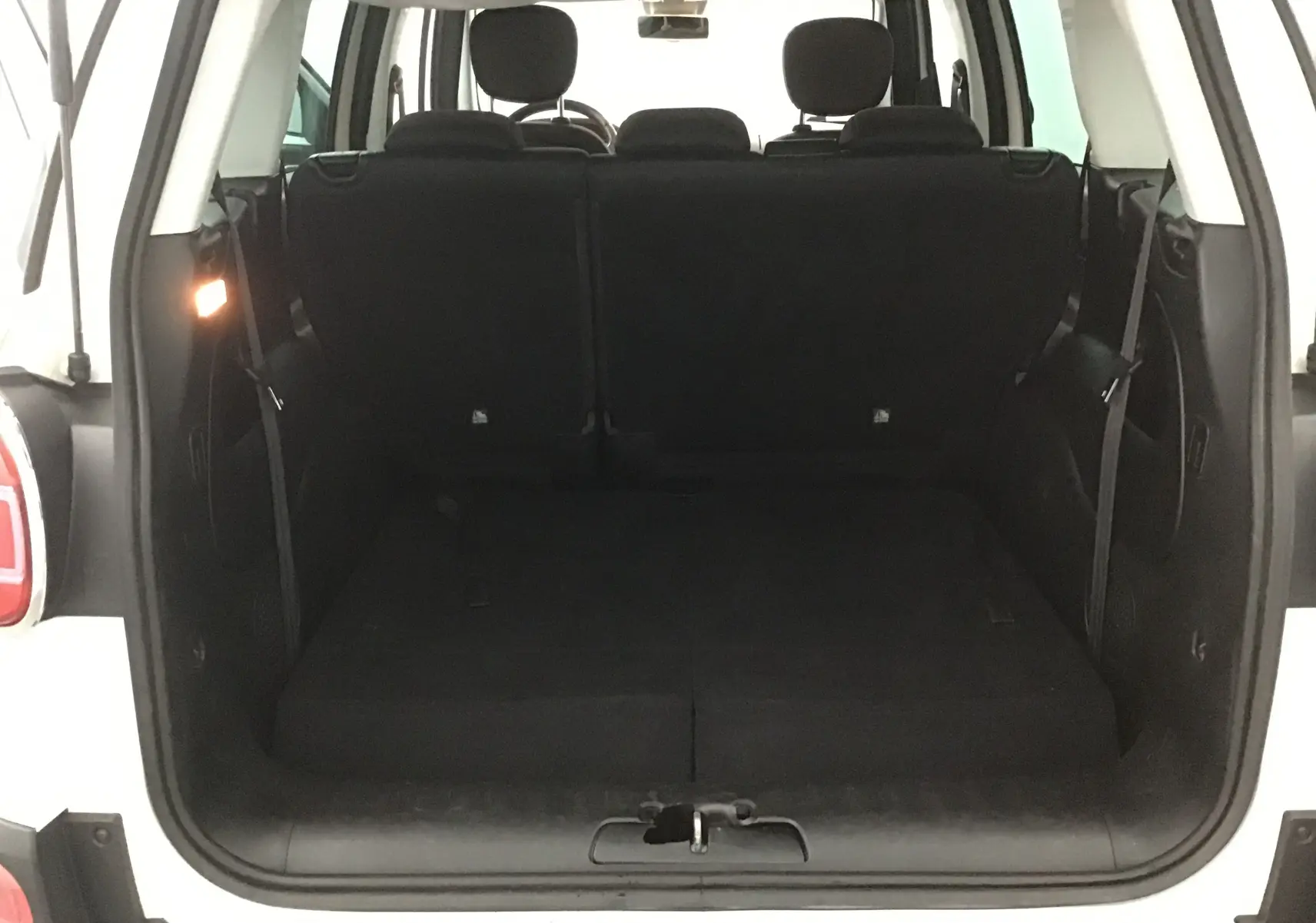 Coffre ouvert vu de l'arrière d'une FIAT 500L blanche, montrant les sièges arrière et l'espace de chargement.