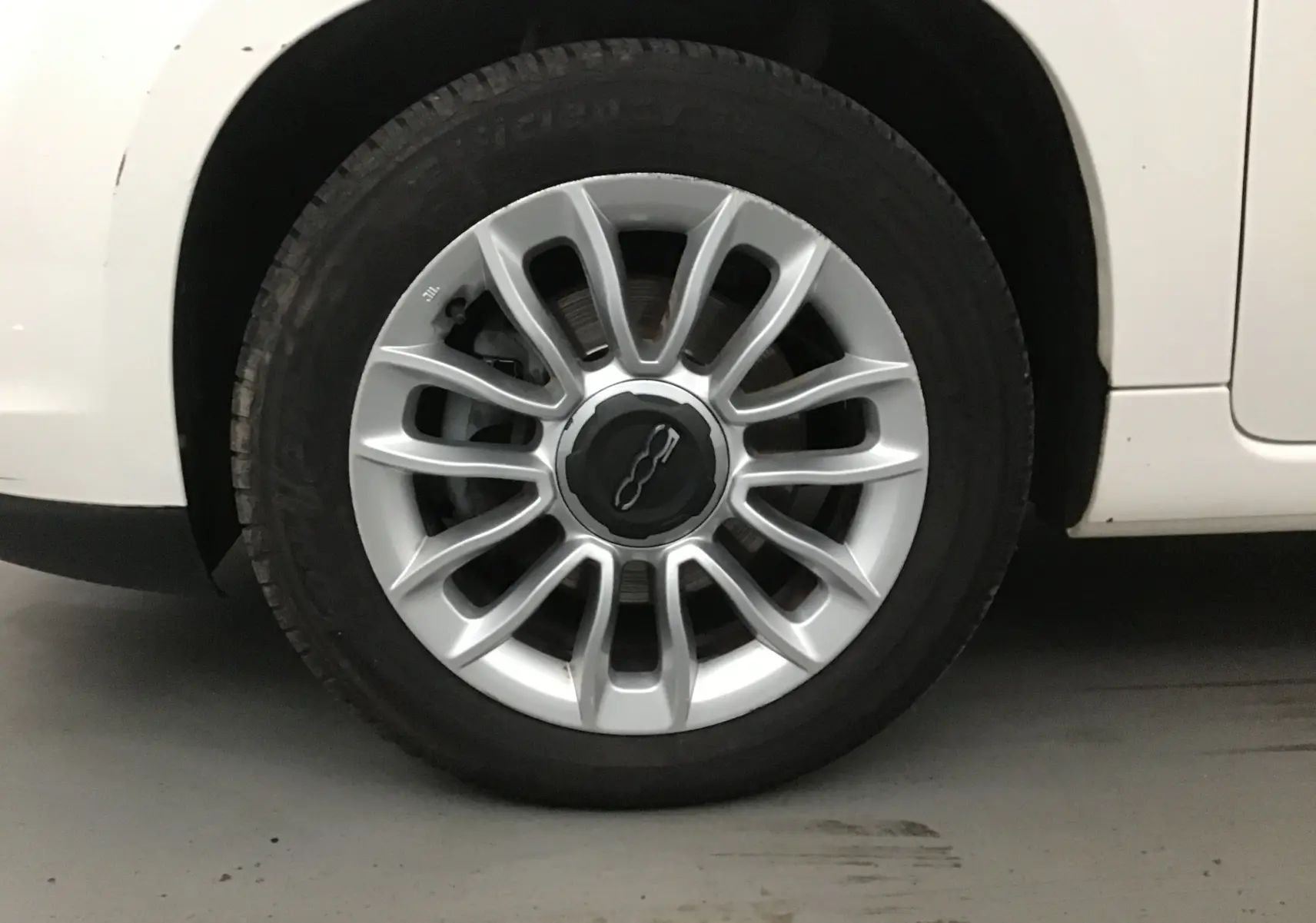 Gros plan sur la roue avant droite d'une FIAT 500L blanche, avec jante alliage argentée et logo central noir.