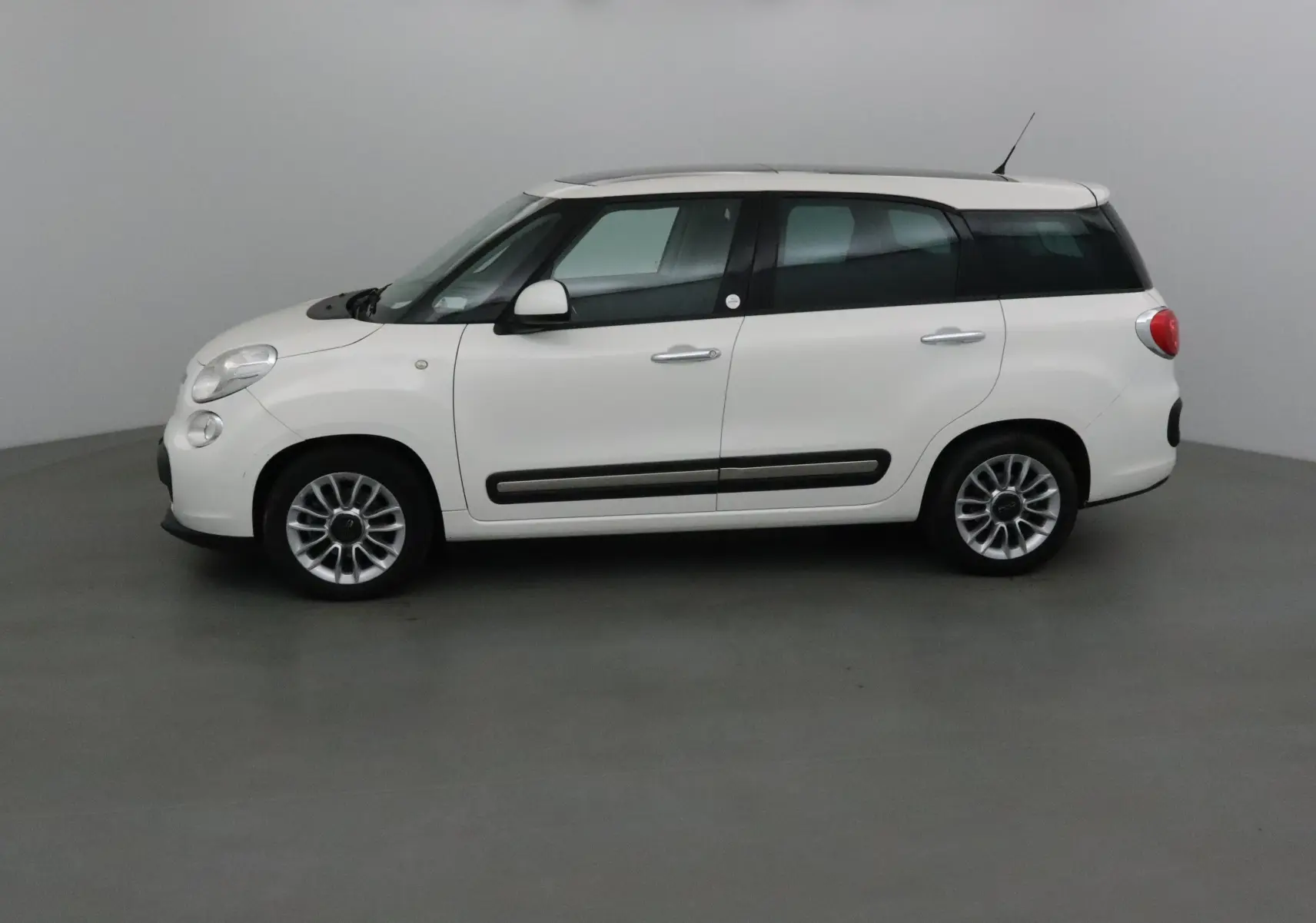 Profil côté gauche d'une FIAT 500L blanche de 2015 avec lunette arrière surteintée dans un studio neutre.