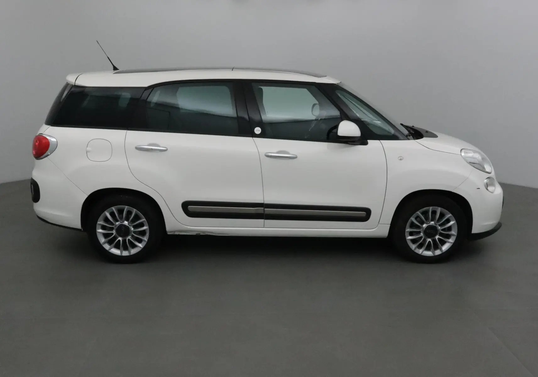 Profil droit d'un FIAT 500L blanc de 2015 avec lunette arrière surteintée et jantes alliage 16 pouces.