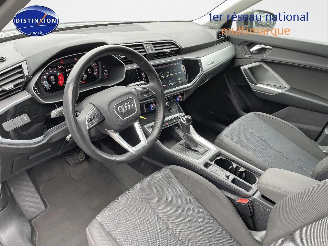 Intérieur de l'Audi Q3 2019 vu côté conducteur, tableau de bord numérique et sièges tissu gris visibles.