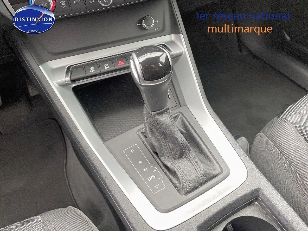 Le levier de vitesses automatique de l'Audi Q3 35 TFSI 150CH en gros plan, avec console grise et sellerie tissu noire.