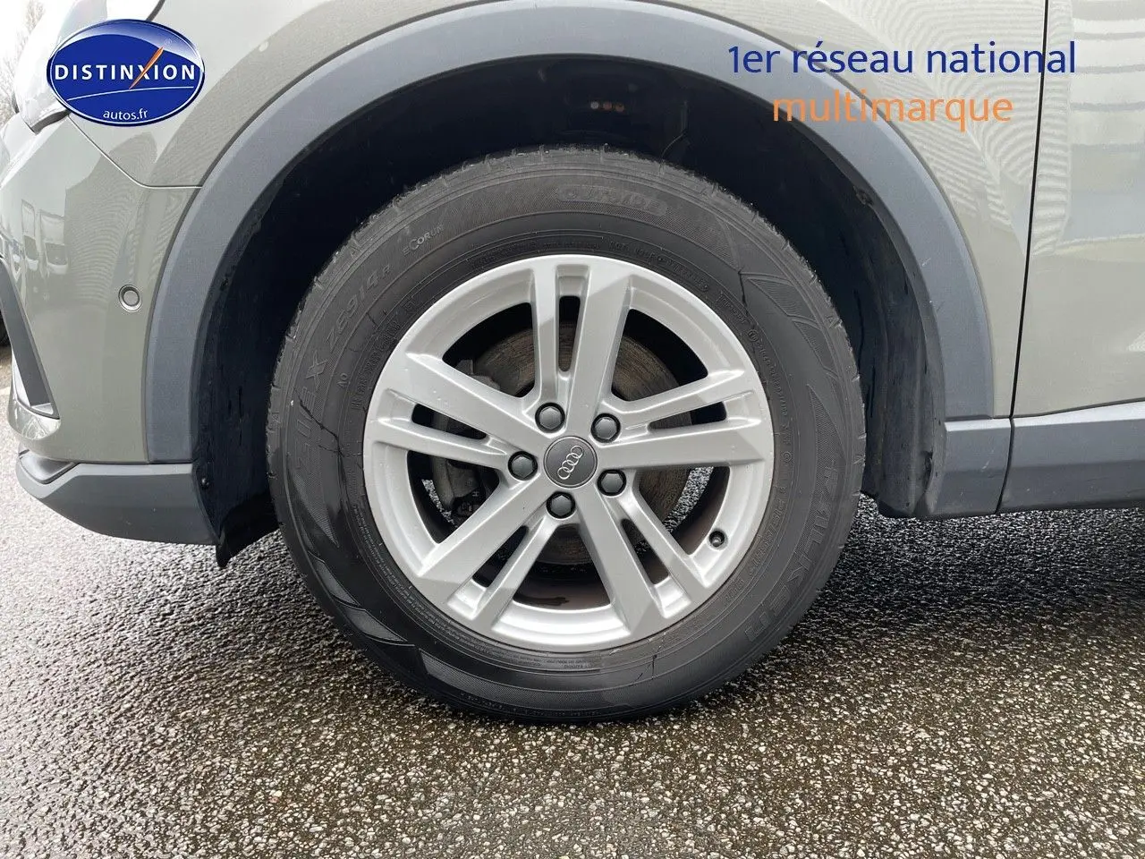 Gros plan sur la roue avant gauche d'un Audi Q3 gris Chronos métal, mettant en valeur la jante alliage 5 branches.