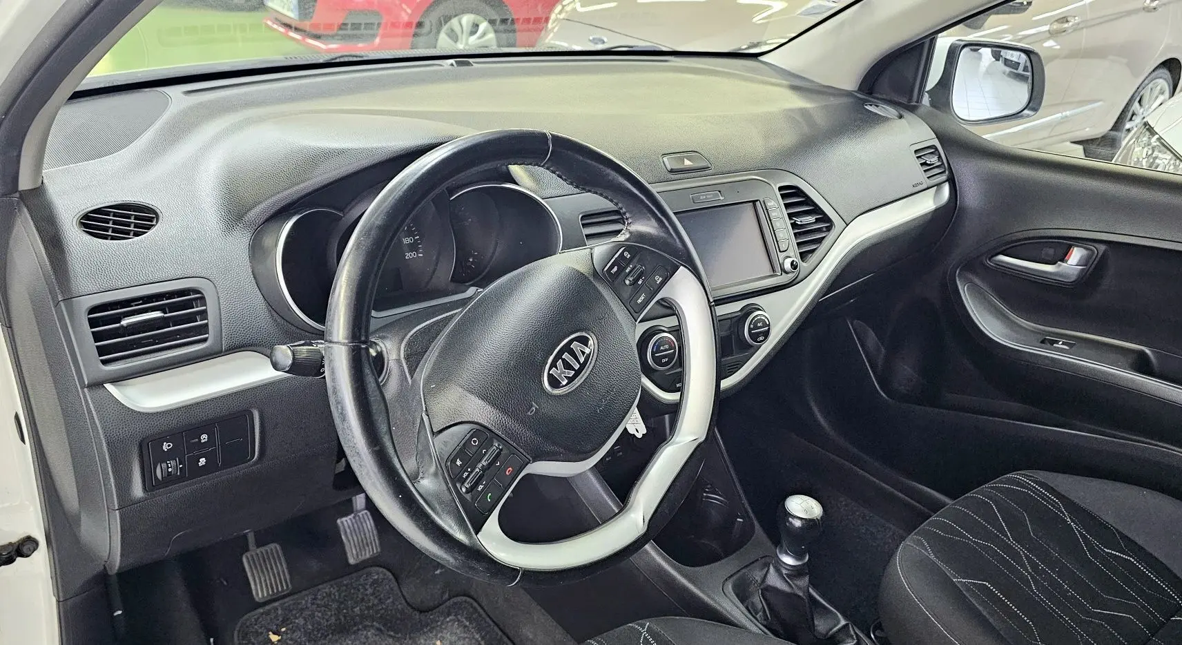Intérieur de la KIA PICANTO blanche 2016, vue côté conducteur sur le tableau de bord et volant multifonction.