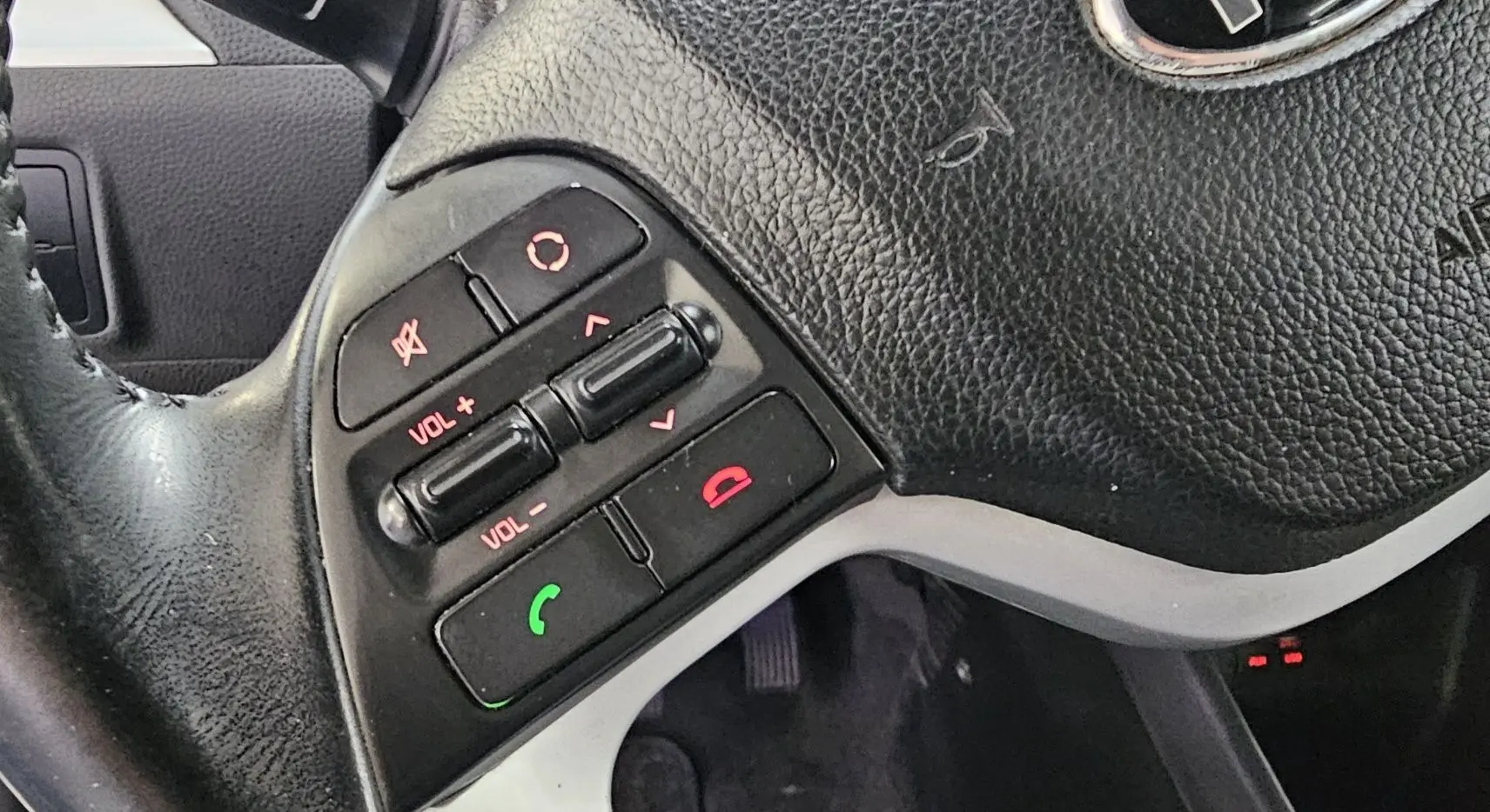 Gros plan sur les commandes audio et téléphone au volant en cuir noir d'une KIA Picanto blanche de 2016.