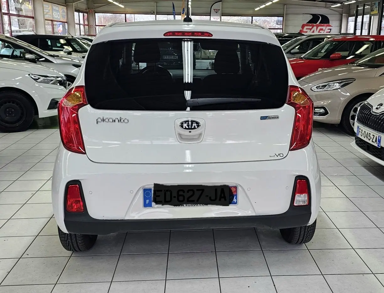 Vue arrière d'une KIA Picanto blanche de 2016, avec feux rouges et plaque d'immatriculation française visible.