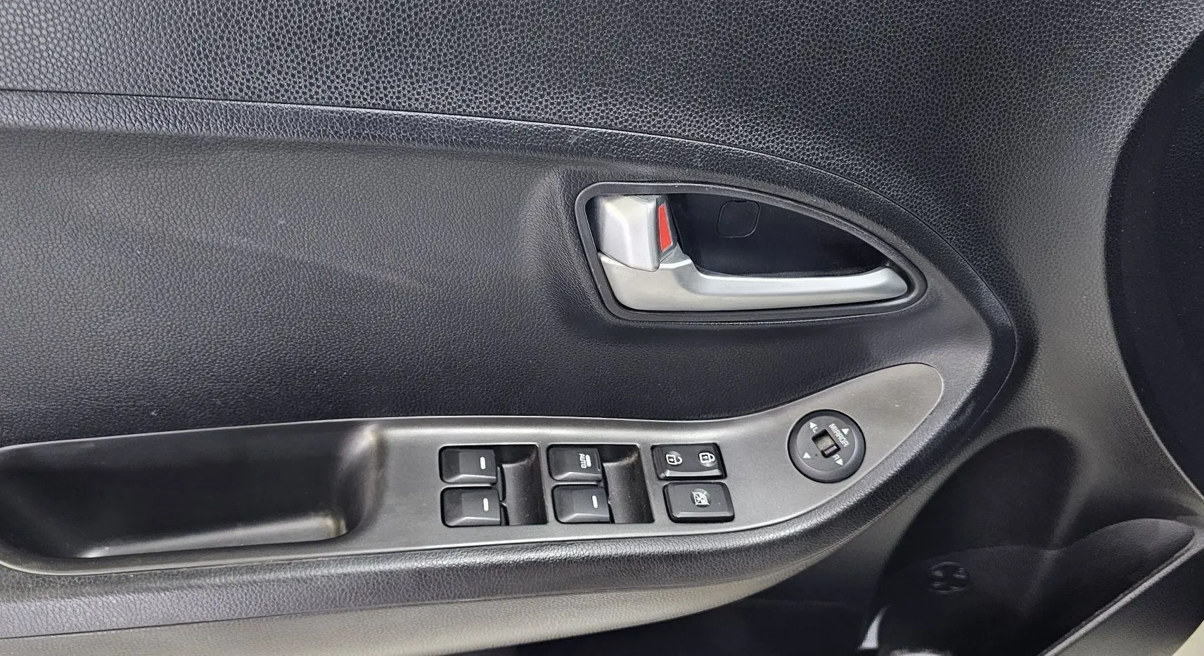 Poignée intérieure côté gauche de la porte d’une Kia Picanto blanche, avec commandes de vitres et rétroviseurs électriques.