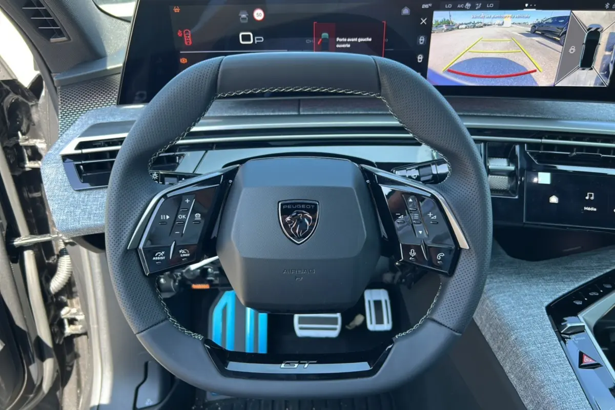 Vue rapprochée du volant cuir multifonctions Peugeot 3008 Hybrid GT 2025 avec tableau de bord digital et caméra de recul affichée.