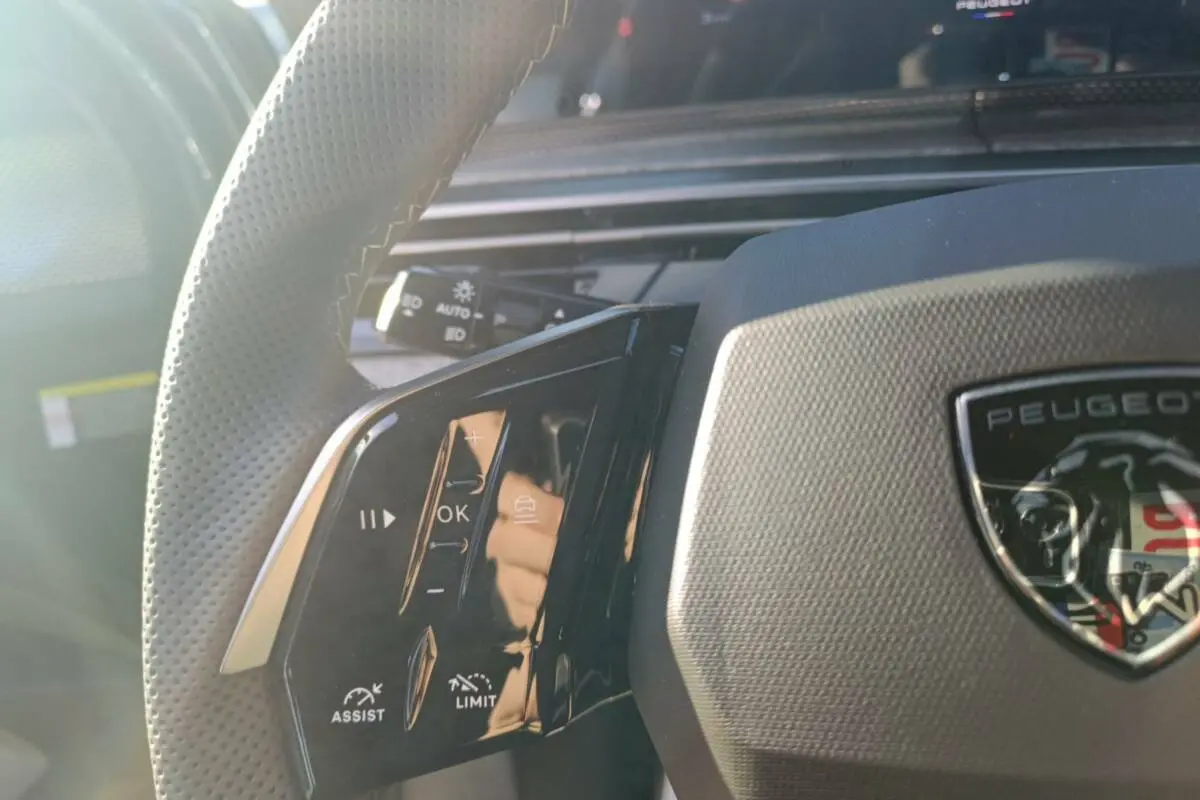 Gros plan sur le volant cuir perforé côté gauche du Peugeot 3008 Hybrid bleu ingaro avec commandes multifonctions.