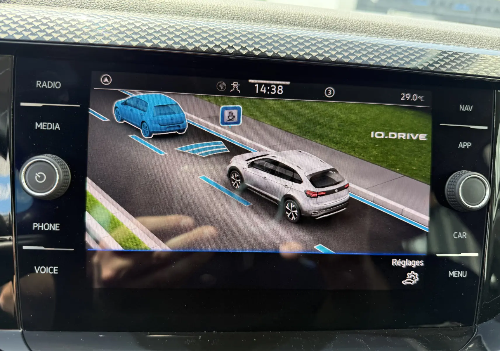 Affichage numérique intérieur montrant une Volkswagen Taigo gris reflet d'argent en vue 3/4 arrière droite avec assistance IQ.DRIVE active.