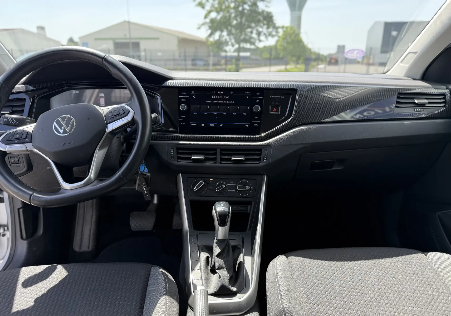 Vue intérieure avant du Volkswagen Taigo gris, mettant en valeur le volant multifonction, l’écran tactile central et la console avec boîte automatique.