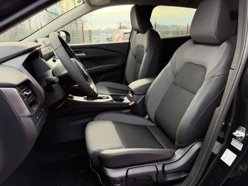 Vue intérieure côté conducteur du Nissan Qashqai Hybrid e-POWER 2025, sièges tissu gris et console centrale moderne.