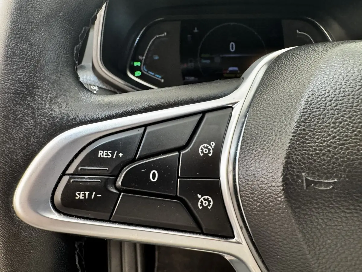 Gros plan sur les commandes du régulateur de vitesse sur le volant cuir noir de la Renault Clio Business E-TECH 140 gris clair.