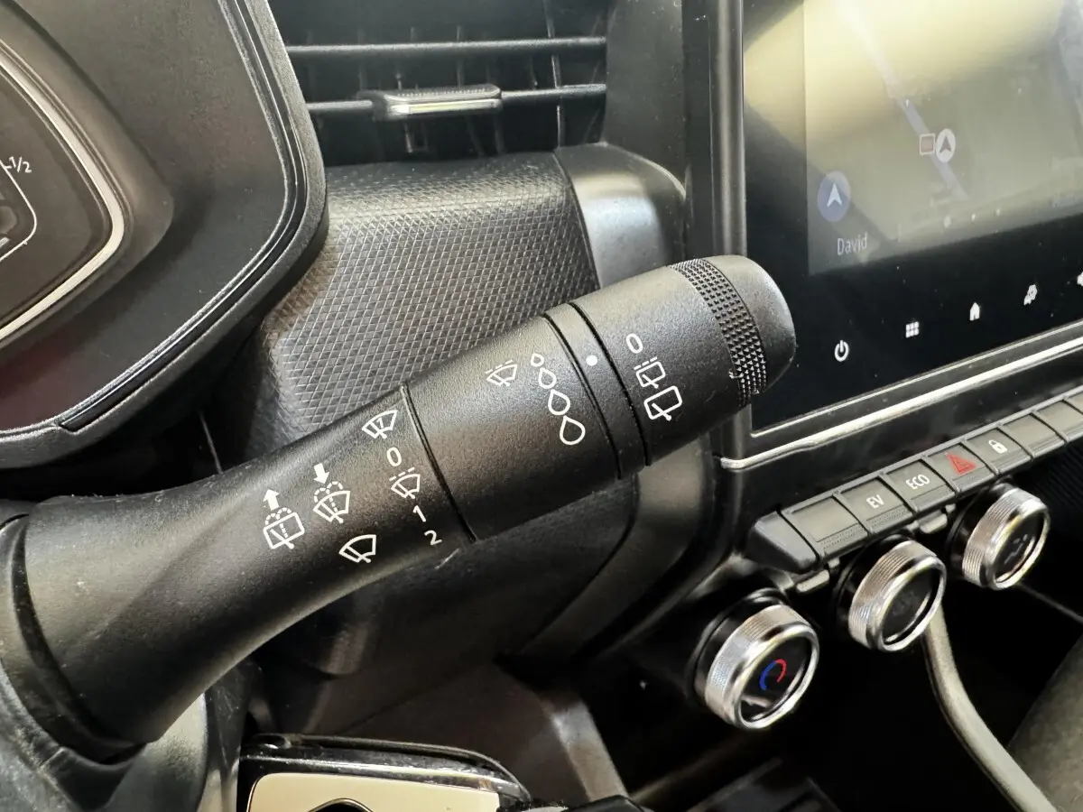 Gros plan sur la commande d’essuie-glace noire et le tableau de bord avec écran tactile dans une Renault Clio Business E-TECH gris clair.
