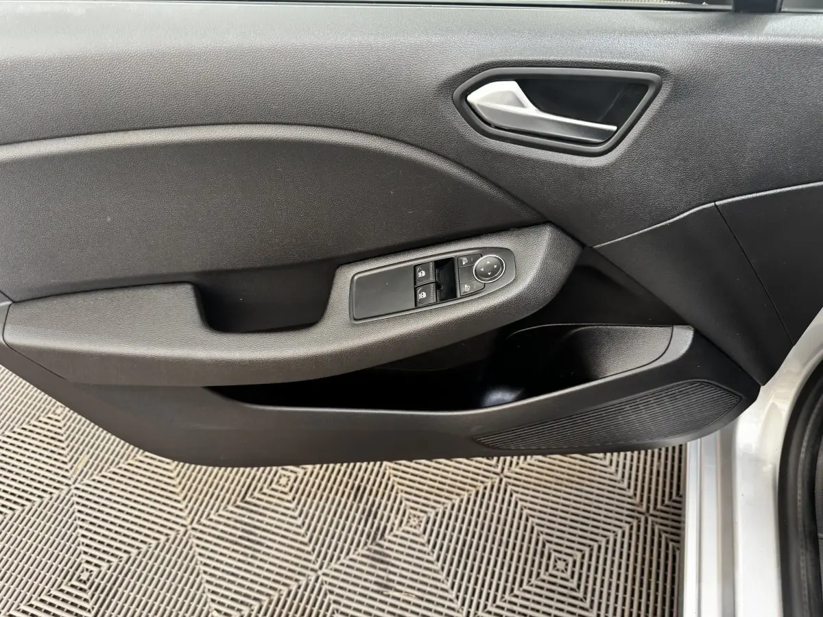 Vue intérieure côté gauche de la porte avant d'une Renault Clio Business E-TECH 140 gris clair avec commandes de vitres et poignée argentée.