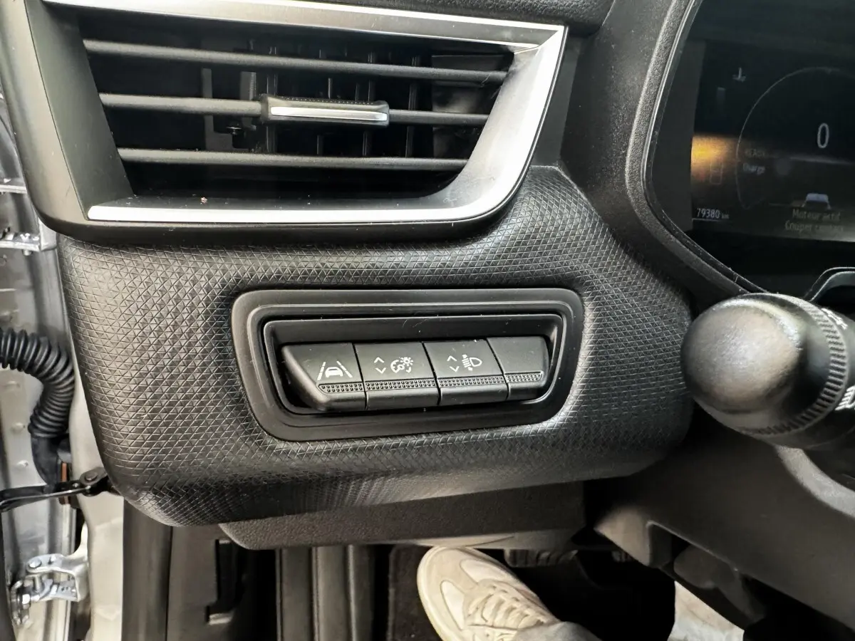 Gros plan sur les commandes de réglage d'assistance et phares à gauche du tableau de bord gris clair de la Renault Clio Business E-TECH 2022.