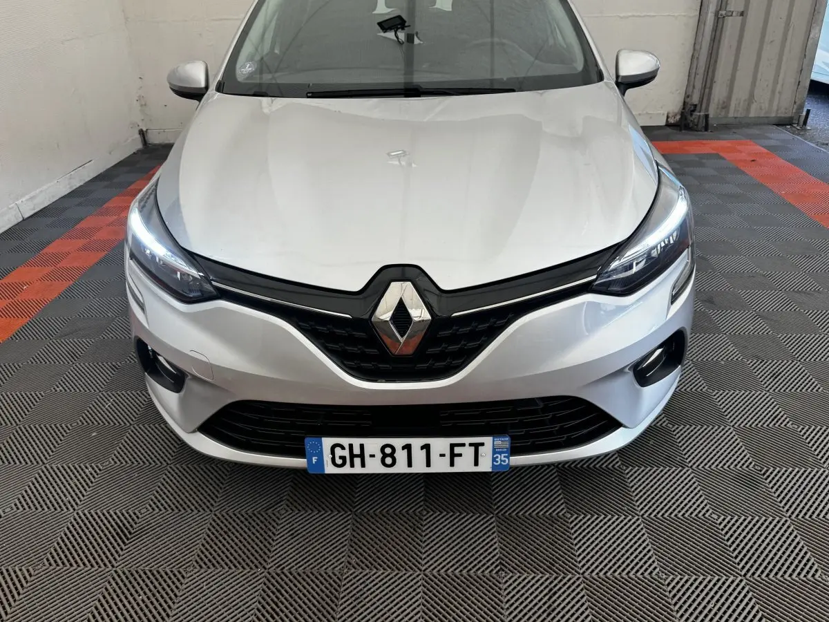 Vue de face d'une Renault Clio Business E-TECH 140 gris clair avec phares LED allumés sur sol à damier noir et orange.