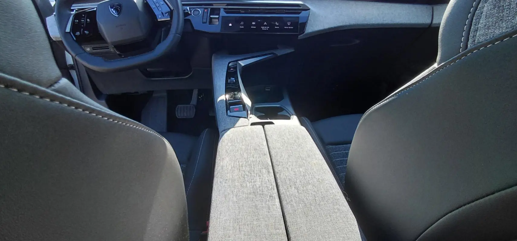 Vue intérieure centrée sur la console centrale et le volant du Peugeot 5008 Hybrid 2025 avec finition tissu gris et noir.