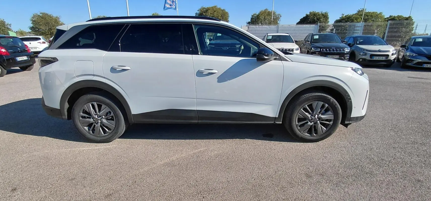 Peugeot 5008 Hybrid blanc vue de profil côté gauche, avec jantes alliage et vitres teintées, stationné en extérieur.