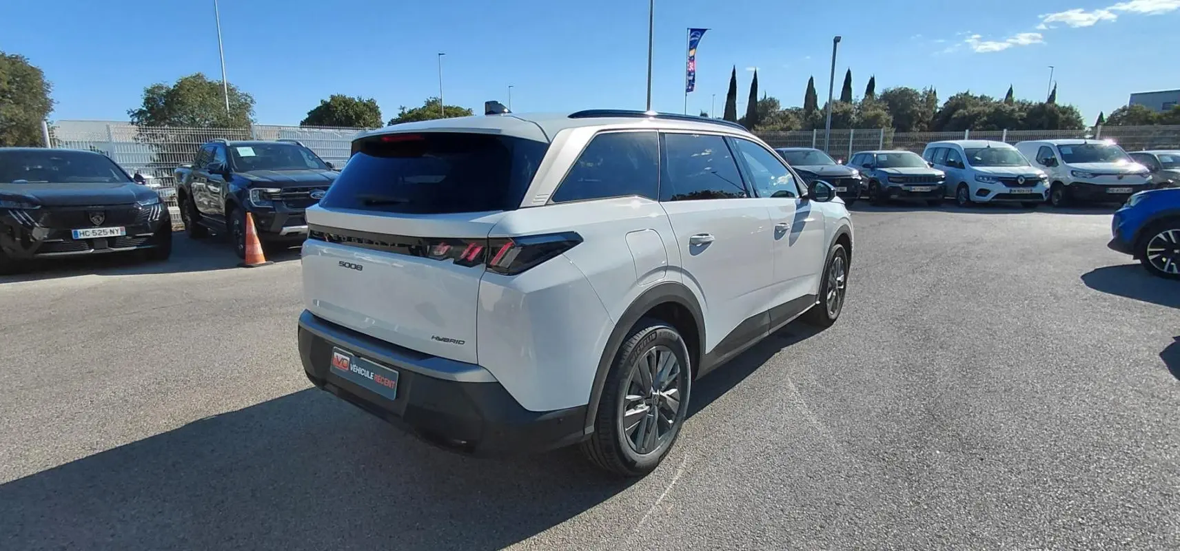 Vue 3/4 arrière droite d’un Peugeot 5008 blanc Hybrid 145 ch 2025, avec feux arrière distinctifs et toit panoramique.