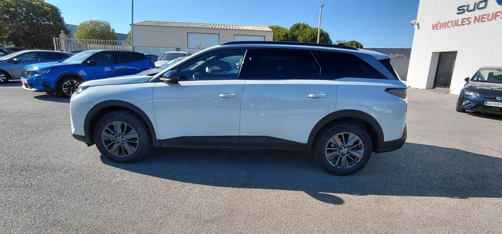 Vue de profil côté gauche du Peugeot 5008 blanc Hybrid 145 ch Allure 2025 garé en extérieur.