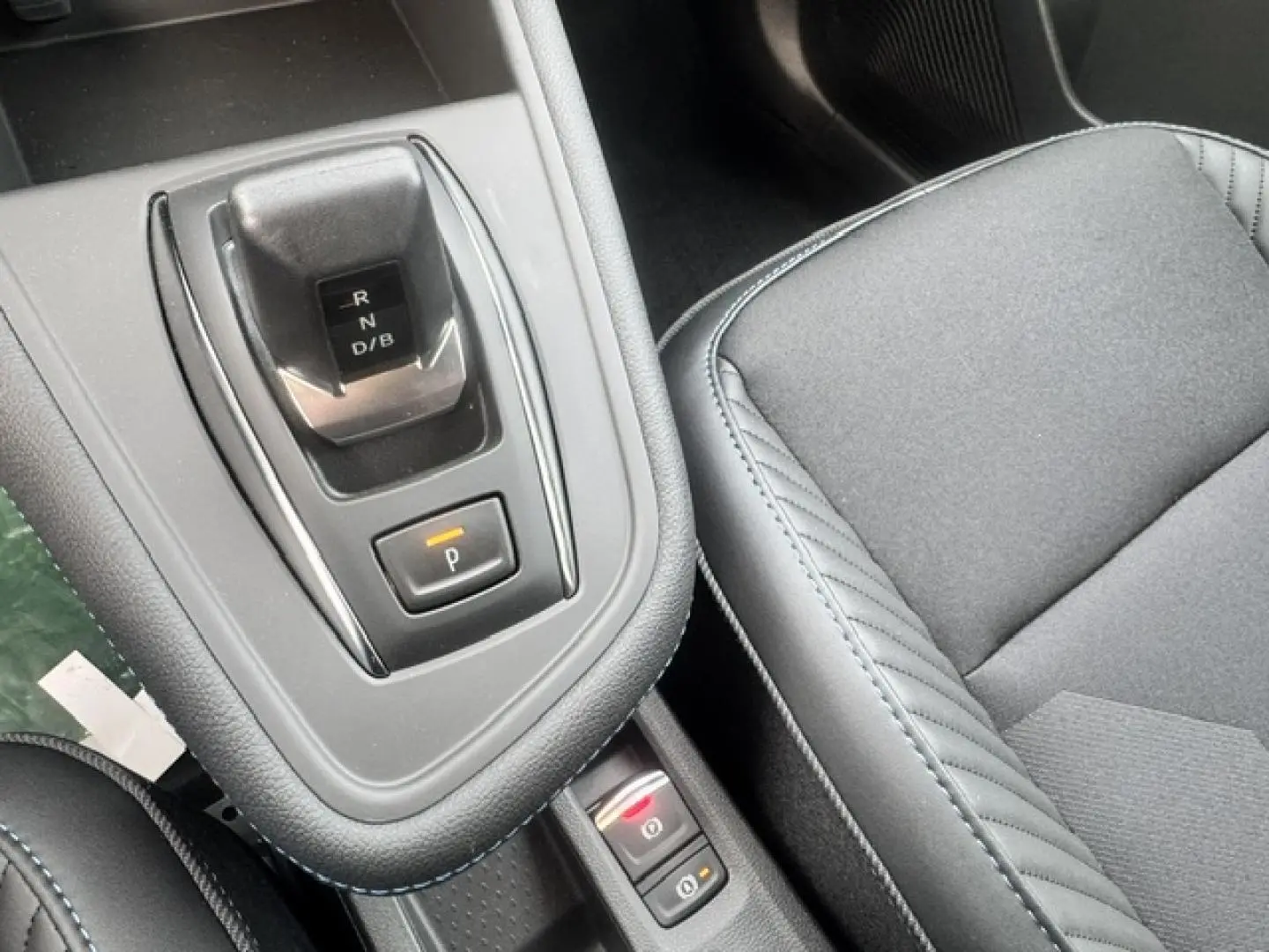 Gros plan intérieur sur la console centrale et siège gris du Renault Symbioz 1.8 E-Tech hybride, avec levier de vitesses automatique.
