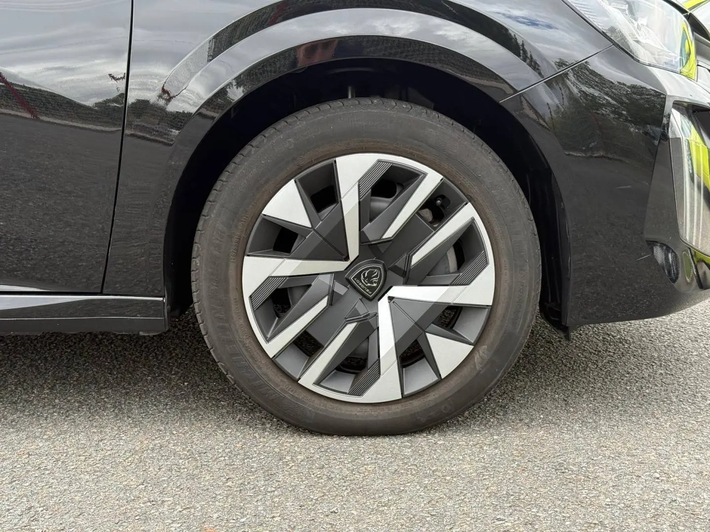 Gros plan sur la roue avant droite d'une Peugeot 208 noire Perla Nera avec jante au design géométrique bicolore.